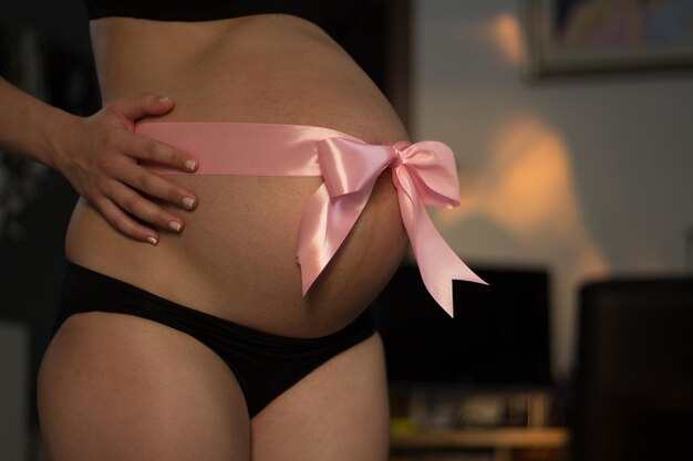 Section médiane d'une femme enceinte avec un nœud attaché sur son ventre à la maison