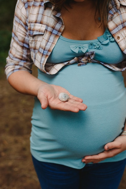 Section médiane d'une femme enceinte tenant une coquille de mer alors qu'elle se tient à l'extérieur