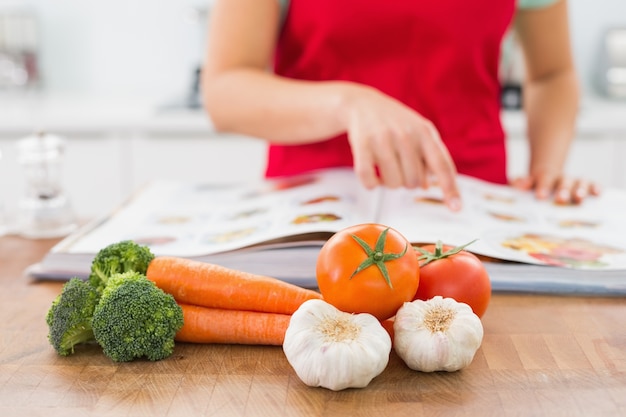 Section médiane d&#39;une femme avec livre de recettes et légumes