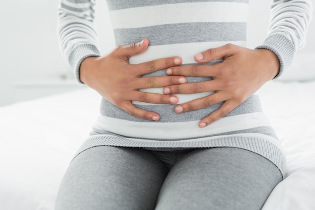 Section médiane d&#39;une femme avec des maux d&#39;estomac assis dans son lit