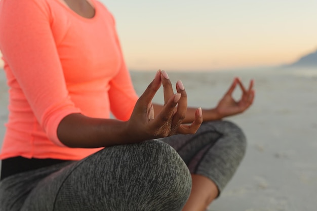 Section médiane d'une femme métisse sur la plage pratiquant le yoga méditant. loisirs en plein air sains au bord de la mer.