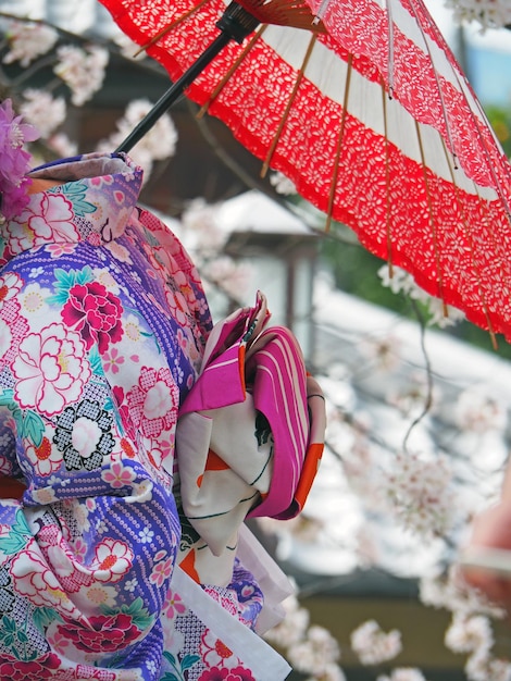 Section médiane d'une femme portant un kimono avec un parapluie rouge contre un cerisier