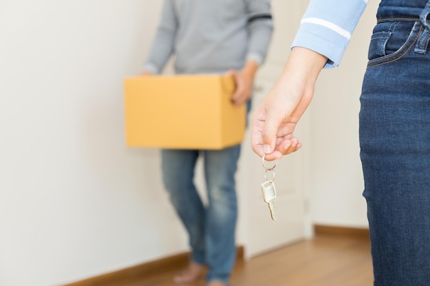 Photo section médiane d'une femme tenant une clé par un homme tenant une boîte en carton à la maison