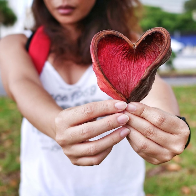 Section médiane d'une femme tenant une forme de cœur alors qu'elle se tient à l'extérieur