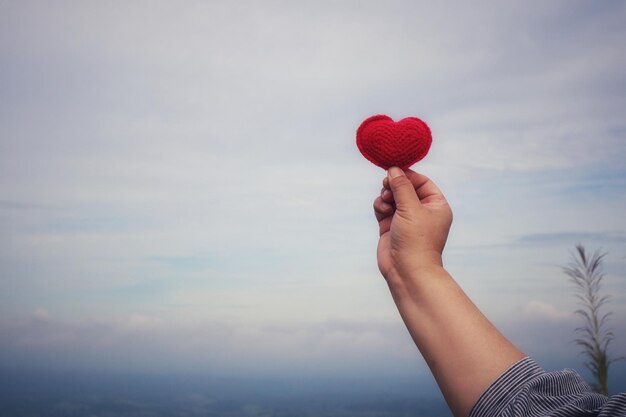 Section médiane d'une femme tenant une forme de cœur contre le ciel