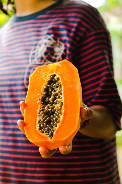 Section médiane d'une femme tenant un fruit de papaye tranché en tranches