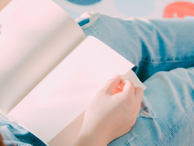 Section médiane d'une femme tenant un livre blanc alors qu'elle est assise à l'intérieur