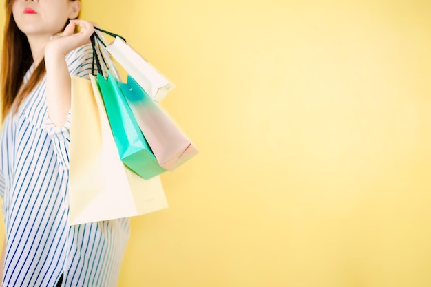 Section médiane d'une femme tenant des sacs d'achat sur un fond jaune