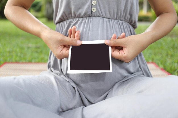 Photo section médiane d'une femme tenant un transfert d'impression instantané alors qu'elle est assise dans un parc