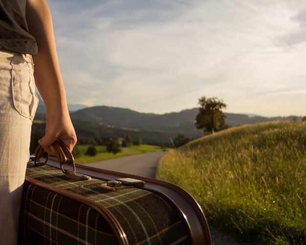 Photo section médiane d'une femme tenant une valise sur la route contre le ciel
