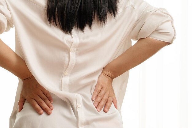 Section médiane de la femme touchant le dos dans la douleur alors qu'elle se tient contre un fond blanc