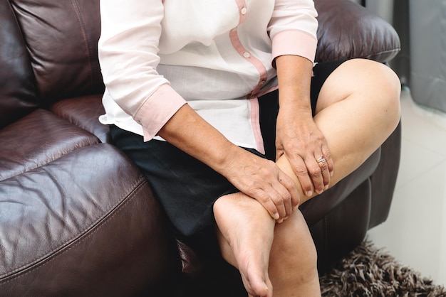 Photo section médiane de la femme touchant la jambe en douleur alors qu'elle est assise sur le canapé