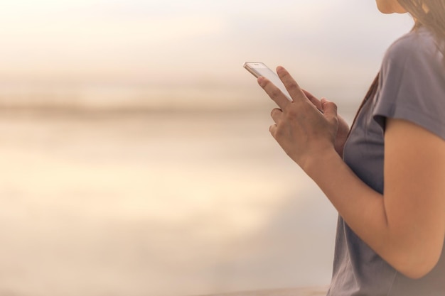Section médiane d'une femme utilisant un smartphone contre le ciel au coucher du soleil