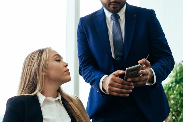 Photo section médiane d'un homme d'affaires montrant son téléphone portable à un collègue au bureau