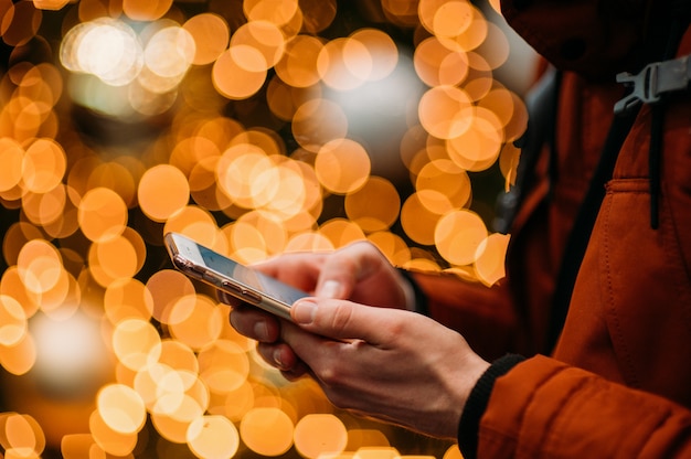 Section médiane de l'homme à l'aide d'un téléphone intelligent contre l'arbre de Noël illuminé.