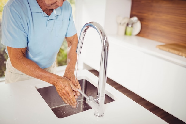 Section médiane d'un homme senior se laver les mains dans la cuisine