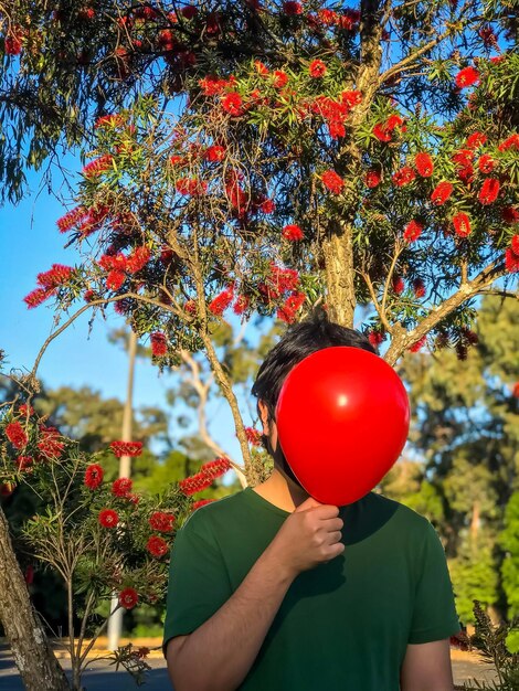 Photo section médiane d'un homme tenant un ballon rouge contre des arbres en fleurs