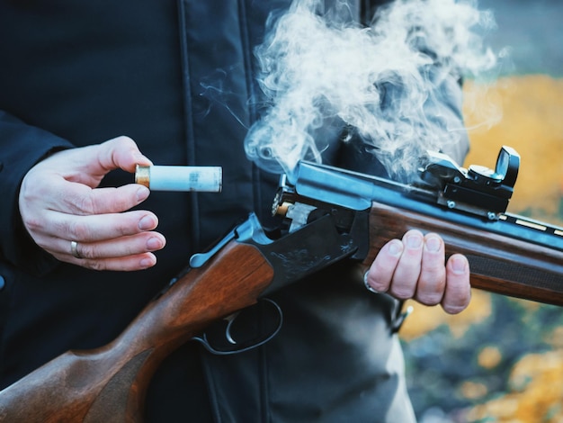 Section médiane d'un homme en train de retirer une balle d'un fusil de chasse alors qu'il se tient à l'extérieur