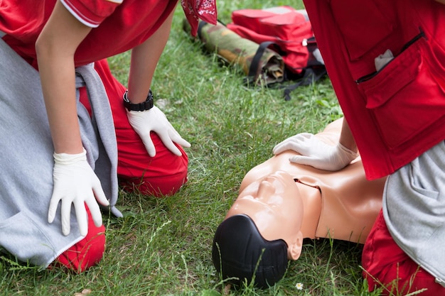 Photo section médiane de l'instructeur enseignant un ambulancier en effectuant une rcp sur un mannequin sur l'herbe