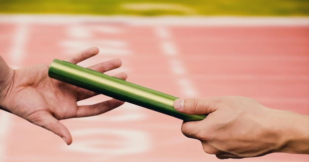 Photo section médiane de la main passant un bâton contre un terrain de sport en arrière-plan