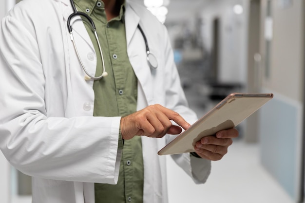 Section médiane d'un médecin de race blanche, debout dans un couloir d'hôpital, regardant une tablette