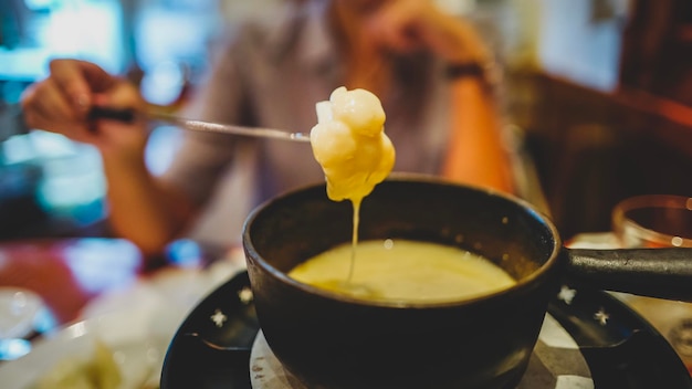 Section médiane d'une personne tenant une fourchette au-dessus d'un bol avec de la fondue au fromage à la maison