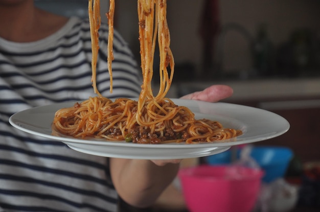 Photo section médiane d'une personne tenant des spaghettis dans une assiette