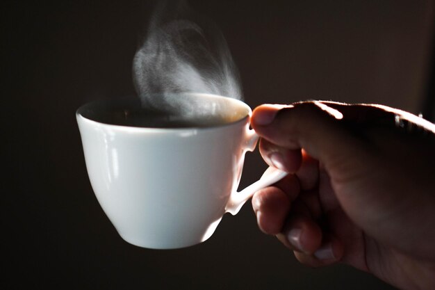 Photo section médiane d'une personne tenant une tasse de café sur un fond noir