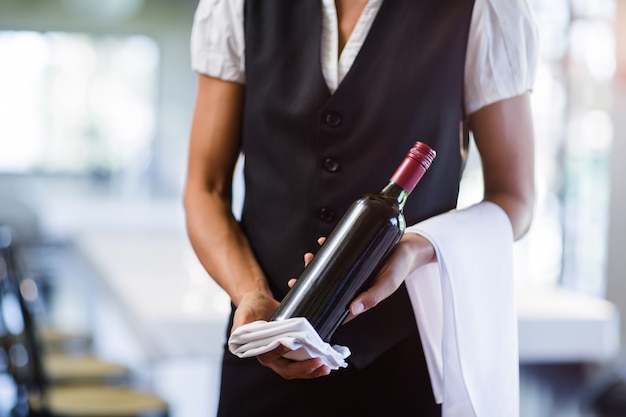 Photo section médiane de la serveuse tenant une bouteille de vin rouge et une serviette