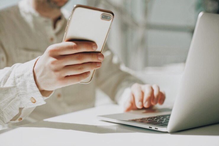 Photo section moyenne d'un homme d'affaires tenant un smartphone et utilisant un ordinateur portable sur la table