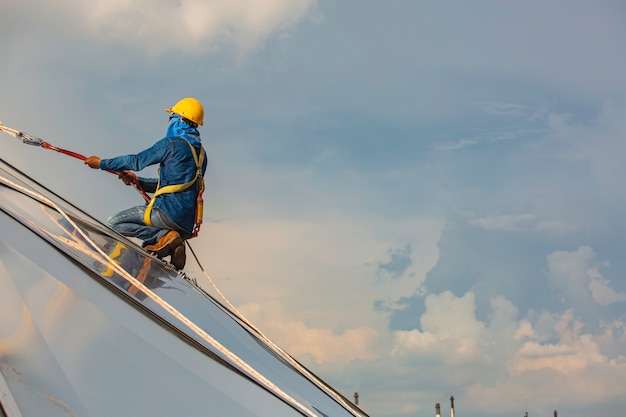 Sécurité de la hauteur d'accès à la corde des travailleurs masculins se connectant à un harnais de sécurité à nœud, se clipsant dans les systèmes de point d'ancrage antichute et de retenue contre les chutes de toit prêts à monter, dôme de réservoir d'huile de chantier de construction