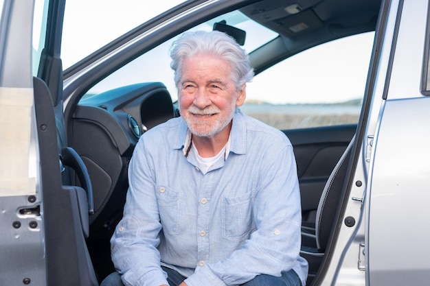 Séduisant adulte vieil homme senior aux cheveux blancs assis dans sa voiture garée en souriant et en détournant les yeux