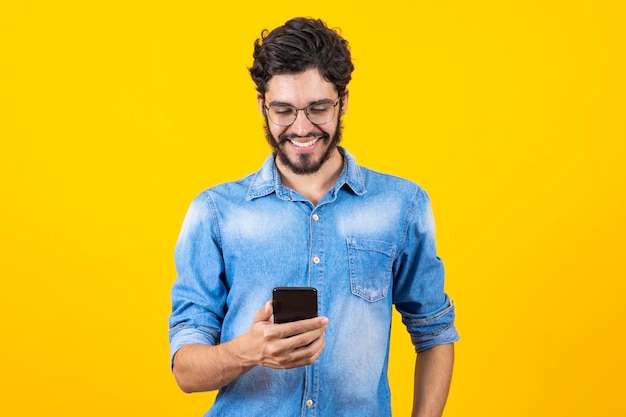 Séduisant beau jeune homme à lunettes à l'aide d'un téléphone portable discutant par SMS sur fond isolé