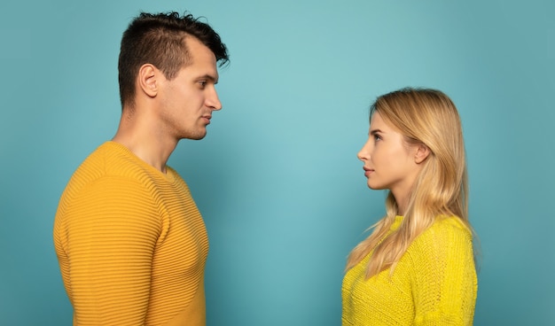 Séduisant un couple en pulls jaunes pose de profil et se regarde dans les yeux avec des sourires radieux