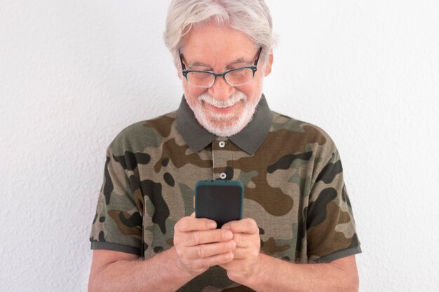 Séduisant homme âgé souriant debout sur fond blanc à l'aide d'un téléphone intelligent pour envoyer des messages. Les personnes âgées utilisent les nouvelles technologies