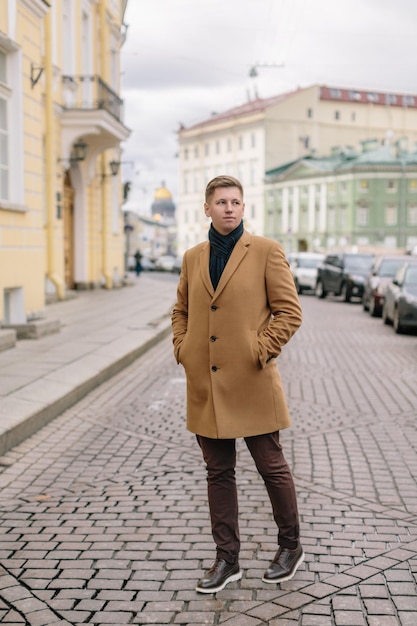 Séduisant homme caucasien blond en manteau beige, pantalon marron et chaussures en cuir foncé Concept de style de vie