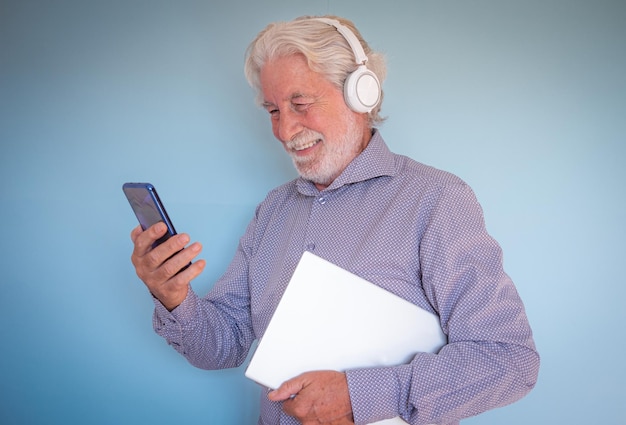 Séduisant homme senior souriant avec un casque utilisant le téléphone dans le chat vidéo tout en tenant un ordinateur portable sous son bras étudiant ou enseignant allant à la leçon