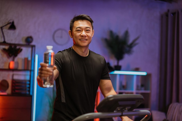 Séduisant jeune homme asiatique sportif tenant une bouteille d'eau fraîche travaillant à courir