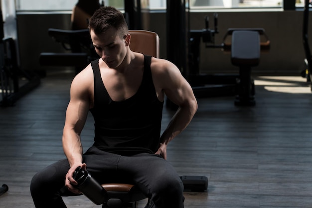 Séduisant jeune homme se reposant dans la salle de sport après l'exercice