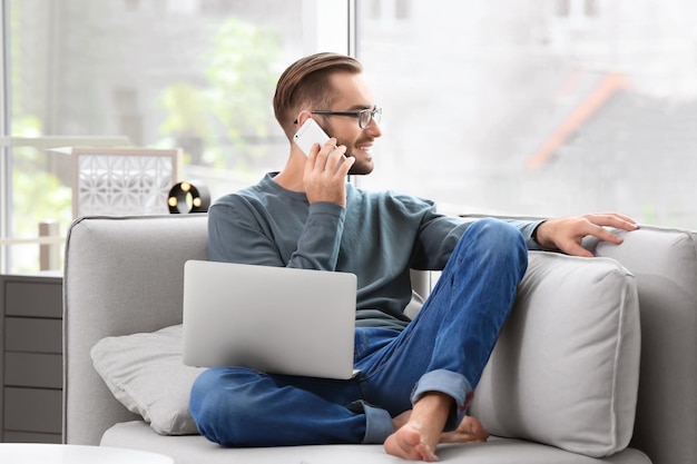Séduisant jeune homme avec smartphone utilisant un ordinateur portable à la maison