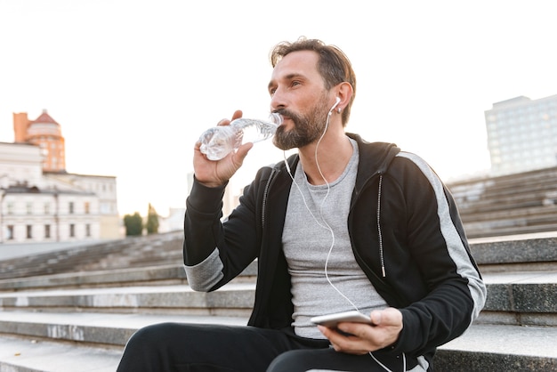 Séduisant sportif dans les écouteurs tenant le téléphone mobile