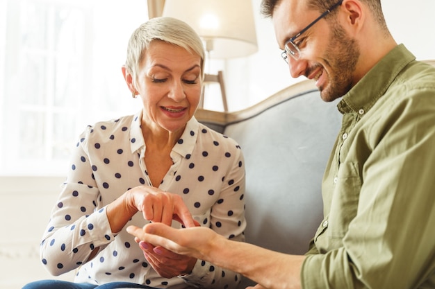 Séduisante blonde senior palm reader prédisant le sourire joyeux aux cheveux noirs de l'avenir du jeune homme de race blanche