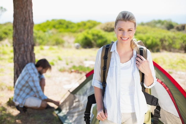 Séduisante blonde souriante à la caméra tandis que son partenaire tente la tente