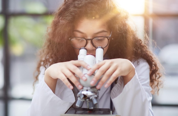 Séduisante femme scientifique regardant à travers un microscope