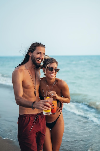 Séduisante jeune couple avec des cocktails alcoolisés marchant sur la plage