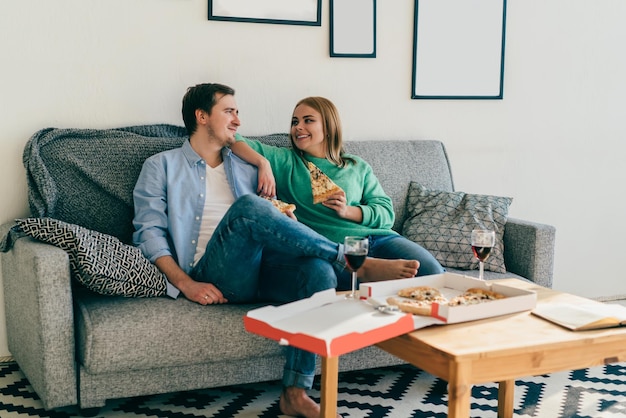 Séduisante jeune couple se détendre sur un canapé en train de manger de la pizza