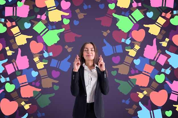 Séduisante jeune femme d'affaires européenne avec les doigts croisés debout sur des icônes colorées abstraites des médias sociaux sur fond flou Concept de rétroaction et de connexion de communication