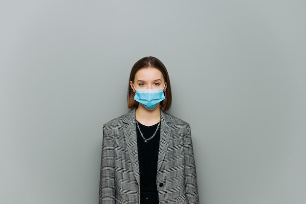 séduisante jeune femme d'affaires en tenues de soirée et masque médical sur le visage sur fond gris