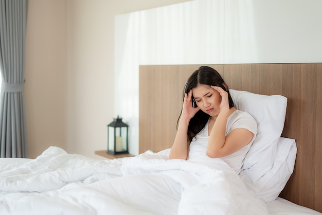 Séduisante jeune femme asiatique se réveille sur son lit, tenant sa main de maux de tête et l'air malheureux et se sentant mal de tête / migraine / stress / malade. Concept de soins de santé pour les femmes.