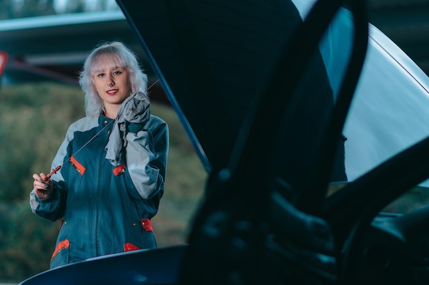 Séduisante jeune femme blonde portant un uniforme de mécanicien automobile et réparant la voiture